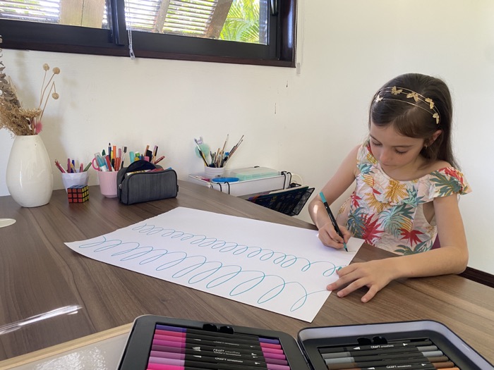 Une enfant trace des boucles sur une grande feuille à l'atelier